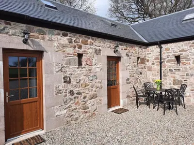 a stone building with a patio with a table and chairs at A Stylish Country Retreat! in Keilour
