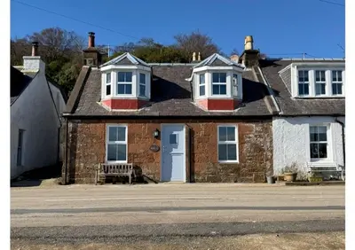 a brick house with a white door and a bench at Eldon Cottage in Isle of Arran