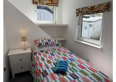 a small bedroom with a bed and two windows at Eldon Cottage in Isle of Arran