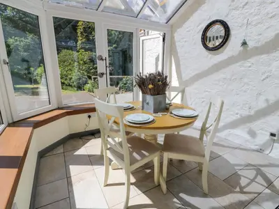 a dining room with a table and chairs and windows at Nithbank Cottage in Thornhill