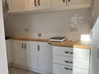 a kitchen with white cabinets and a wooden counter top at Self-contained ground level cottage with hill view in Edinburgh