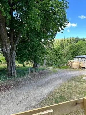 a dirt road with a tree and a building at 27 Glenfinart Caravan Park in Dunoon