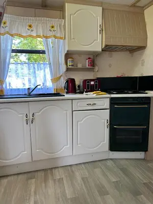 a kitchen with white cabinets and a stove and a window at 27 Glenfinart Caravan Park in Dunoon