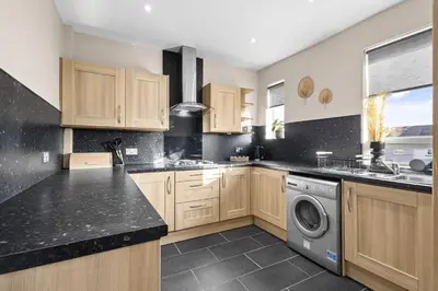 a kitchen with wooden cabinets and a washer and dryer at Welcoming Home in Hurlford, Kilmarnock - Bonnie Lodgings in Hurlford