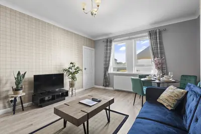 a living room with a blue couch and a table at Welcoming Home in Hurlford, Kilmarnock - Bonnie Lodgings in Hurlford