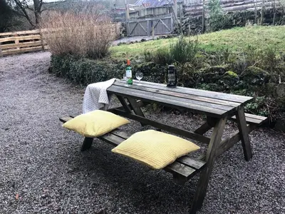 a wooden picnic table with two yellow pillows on it at Corlae Cottage, mountain and forest views in Carsphairn