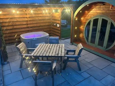 a patio with a table and chairs and a tub at Barnharrow Holiday Pods - Rose Glamping Pod with Hot Tub & Fire Pit in Balminnoch