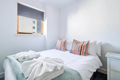 a white bedroom with a bed with a window at Argyle Street Apartments in Glasgow