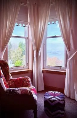a living room with a chair and two windows at No 8 Lomond Castle in Luss