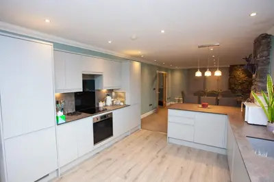 a kitchen with white cabinets and a living room at 5 Bed Family Home Lochwinnoch in Lochwinnoch
