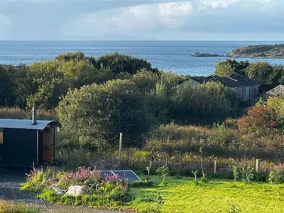 a small building in a field next to the water at The Shepherd's Hut in Craighouse