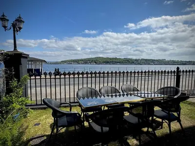 a picnic table with chairs and a fence next to the water at The Old Church Isle of Bute in Port Bannatyne