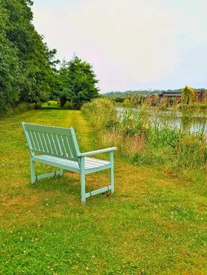 a bench sitting in the grass next to a lake at Lakeside Lodge Retreat, with Roof Deck - Golf & Spa, Gleneagles