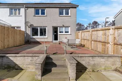 a house with a retaining wall and a fence at Free Parking - Central - Sleeps 8 - 3 Bedrooms in Livingston
