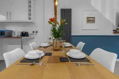 a wooden table with white plates and glasses on it at Free Parking - Central - Sleeps 6 - 2 Bedrooms in East Calder