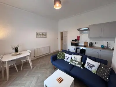 a living room with a blue couch and a kitchen at Balloch But & Ben in Balloch
