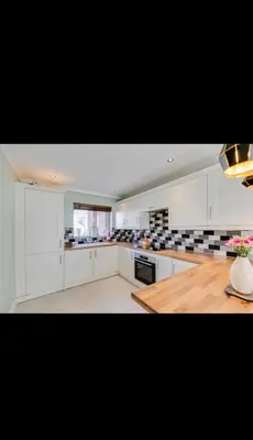 a kitchen with white cabinets and a wooden table at Modern home Close to all Cardiff venues in Moffat