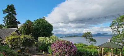 a house with flowers and a gazebo and a lake at Bruach Lodge in Balloch