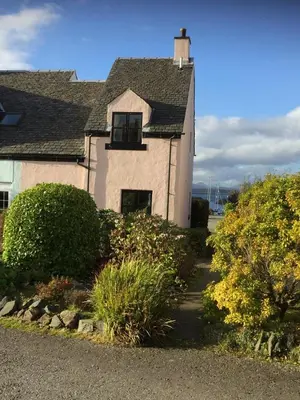 a white house with a window and bushes at Morvern Cottage in Craobh Haven
