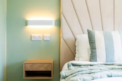 a bedroom with a bed and a nightstand and a lightswitch at Bright & Modern 3-Bed House Next To Glasgow Airport in Abbotsinch