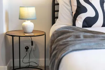 a table with a lamp on it next to a bed at No15 Ellis House - Donnini Apartments in Kilmarnock