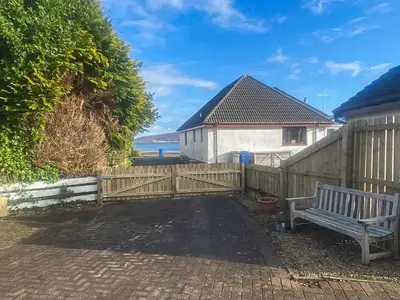 a wooden fence with a bench in front of a house at Riverside Cottage in Lamlash