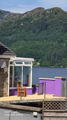 a purple house with a deck next to the water at Jenny's Bay with Hot Tub in Lochgoilhead
