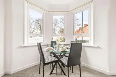 a dining room with a table and chairs and windows at Cosy and Bright 3-Bedroom Flat in Glasgow