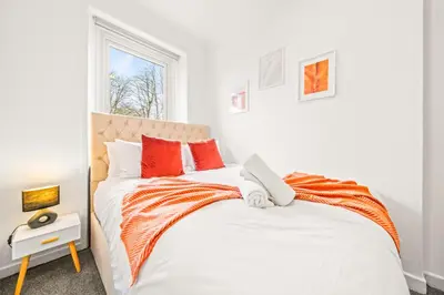 a white bedroom with an orange and white bed at Cosy and Bright 3-Bedroom Flat in Glasgow