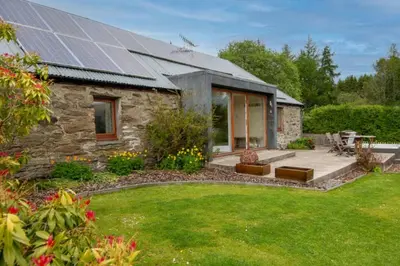 a stone house with solar panels on the roof at Sams Cottage with Loch Tay Vistas and Hot Tub in Lawers