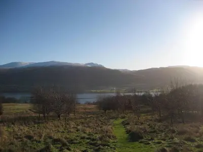 a field with a lake and mountains in the background at Ben Lawers Rest Cabin - Hot Tub and Loch Tay Vistas in Lawers