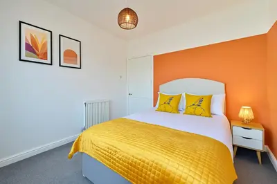 a bedroom with a bed with an orange wall at Walk to Hydro and SEC Modern 3BR Free Parking in Glasgow
