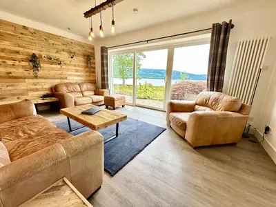 a living room with leather furniture and a large window at Avenue Cottage, Inveraray in Inveraray