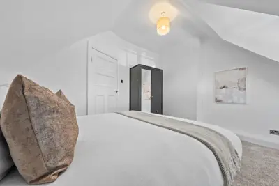 a white bedroom with a bed with a pillow on it at Kirkstyle Cottage in Coatbridge