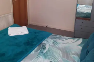 a bedroom with a bed with a blue blanket and a dresser at gourock blissful apartment with 3 bedrooms in Gourock