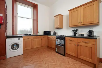 a kitchen with wooden cabinets and a washing machine at Family and Group Stay 2BR by Park Sleeps 7 in Glasgow