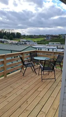 a patio with two chairs and a table on a deck at Three Lochs Holiday Park- Lochwood Caravan in Newton Stewart
