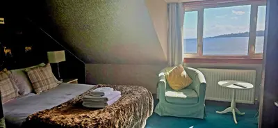 a bedroom with a bed and a chair and a window at The Bay Rooms at Glenisle Hotel in Lamlash