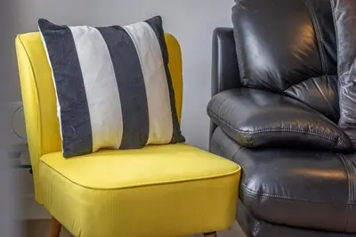 a yellow chair with a pillow next to a brown leather chair at Modern 2-Bedroom Home near Glasgow & Edinburgh in Airdrie