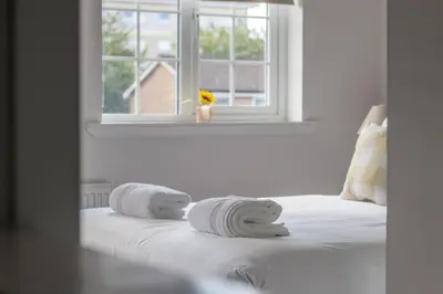 a white bedroom with towels on a bed with a window at Modern 2-Bedroom Home near Glasgow & Edinburgh in Airdrie