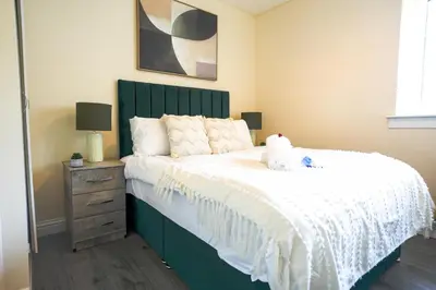 a bedroom with a large bed with a green headboard at 3 BDR House By Caledonia Luxe Stays Short Lets & Serviced Accommodation Wishaw in Wishaw