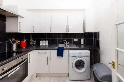 a kitchen with white cabinets and a washer and dryer at Cosy Central Apartment by the Meadows 11 in Edinburgh
