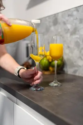 a person pouring orange juice into two glasses on a counter at Finnieston 1BR - Walk to Hydro & SEC - Parking in Glasgow