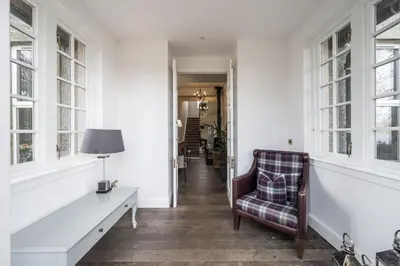 a hallway with a chair and a table and windows at Cairns Farmhouse in Kirknewton