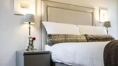 a bedroom with a white bed with a large headboard at Cairns Farmhouse in Kirknewton