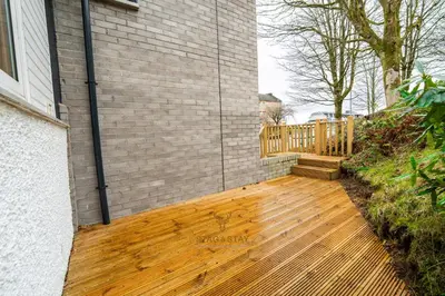 a porch with a wooden deck next to a brick building at Stag & Stay- Waterlillie - Contractor friendly, Fast WiFi in Port Glasgow