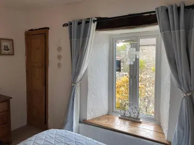 a bedroom with a window with blue curtains at Oronsay, 2 Weint End Cottages, Great Urswick, Ulverston Cumbria LA120SP in Moffat