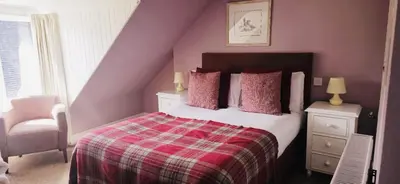 a bedroom with a bed with pink walls and a chair at Glenisle Hotel in Isle of Arran