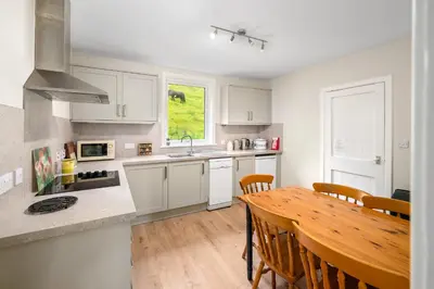 a kitchen with white cabinets and a wooden table at Charming 2-Bed Cottage on Tranquil Raera Farm in Kilninver