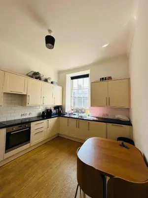 a kitchen with white cabinets and a wooden table at Cozy Room In Sauchiehall Street in Glasgow